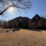 Two-Story House With Bare Trees And Equipment On The Ground Indicating Potential Cleaning Or Maintenance Work Being Done