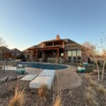 Large House With Patio And Pool Surrounded By Landscaping And Furniture Outdoor Setting With Clear Sky And No Visible People