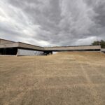 Cloudy Sky Over A Large Commercial Building With A Grassy Area In Front And A Slight Slope Towards The Structure
