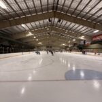 Ice Skating On A Rink With People Enjoying Recreational Activities And Practicing Skating Skills Under A Large Indoor Arena