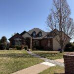 a well maintained brick home with a clear blue sky and neatly trimmed bushes and trees surrounding the yard