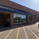 cleaning exterior windows of a retail building with clear skies and well-defined parking lines in front