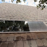 cleaning a dirty skylight on a rooftop with shingles and surrounding foliage