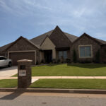 well maintained landscaping on a traditional brick home with a manicured lawn and clear blue sky overhead